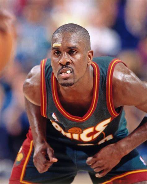 Gary Payton dribbling the ball on the court in a Seattle SuperSonics uniform.