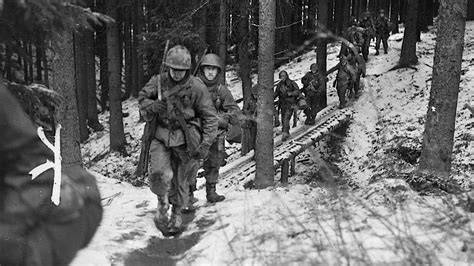 Troops from the 106th Infantry Division navigating through a snowy forest.