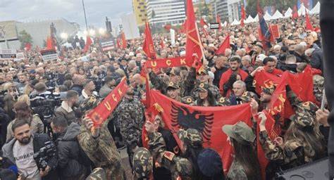 A group of demonstrators holding banners in a central square in Tirana.
