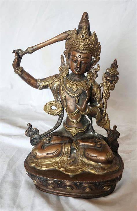 A detailed view of Wenshu Guangfa Tianzun holding a sutra, highlighting his attributes of knowledge.