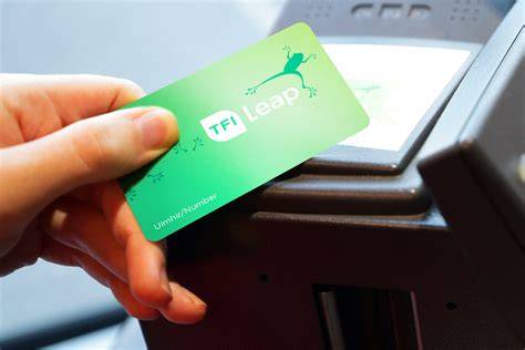 A person is loading money onto their TFI Leap Card at a ticket machine in a transport station.
