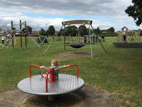 A wide shot of Hethersett Recreation Ground with people walking and children playing.